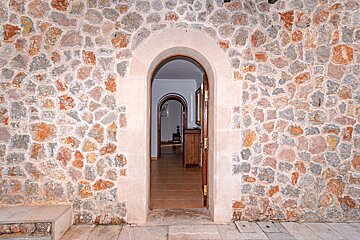A stone wall with an arched doorway leading to a hallway