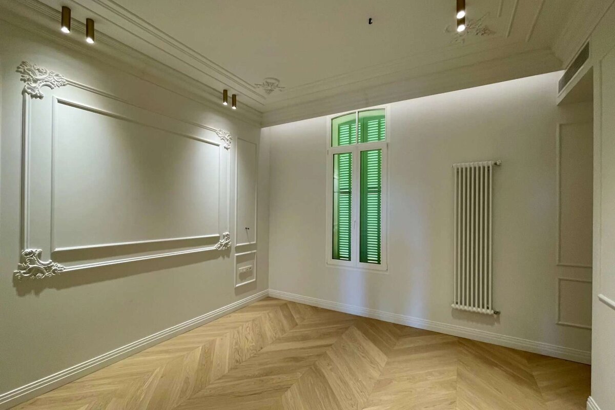 A room with white walls and a window with green shutters