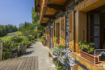 Rustic stone cottage with wooden shutters, flower pots, and a stone patio pathway leading into a lush green garden.