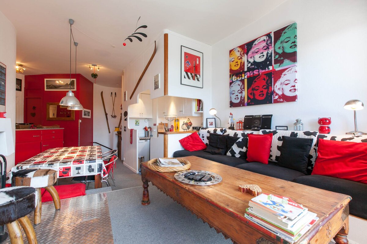 Eclectic, colorful apartment with a red kitchen/dining area and a pop art living room featuring cow print cushions and ski decor.