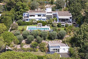 Elevated view of a luxurious white villa with a swimming pool, nestled in a lush, green terraced hillside surrounded by trees.
