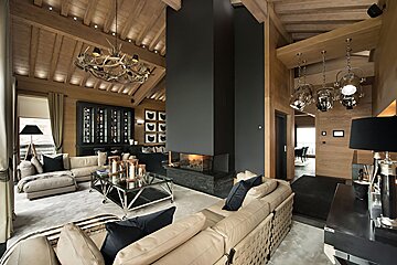 Spacious, luxurious chalet living room with vaulted wood ceiling, antler chandelier, modern fireplace, and stylish neutral furnishings.