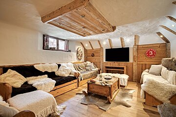 Cozy, rustic chalet living room with wooden walls, sheepskin-covered sofas, and a central coffee table on a hide rug.