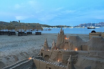 A sand castle is lit up with candles on the beach