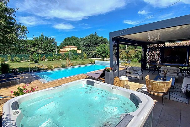 A hot tub sits in front of a large swimming pool