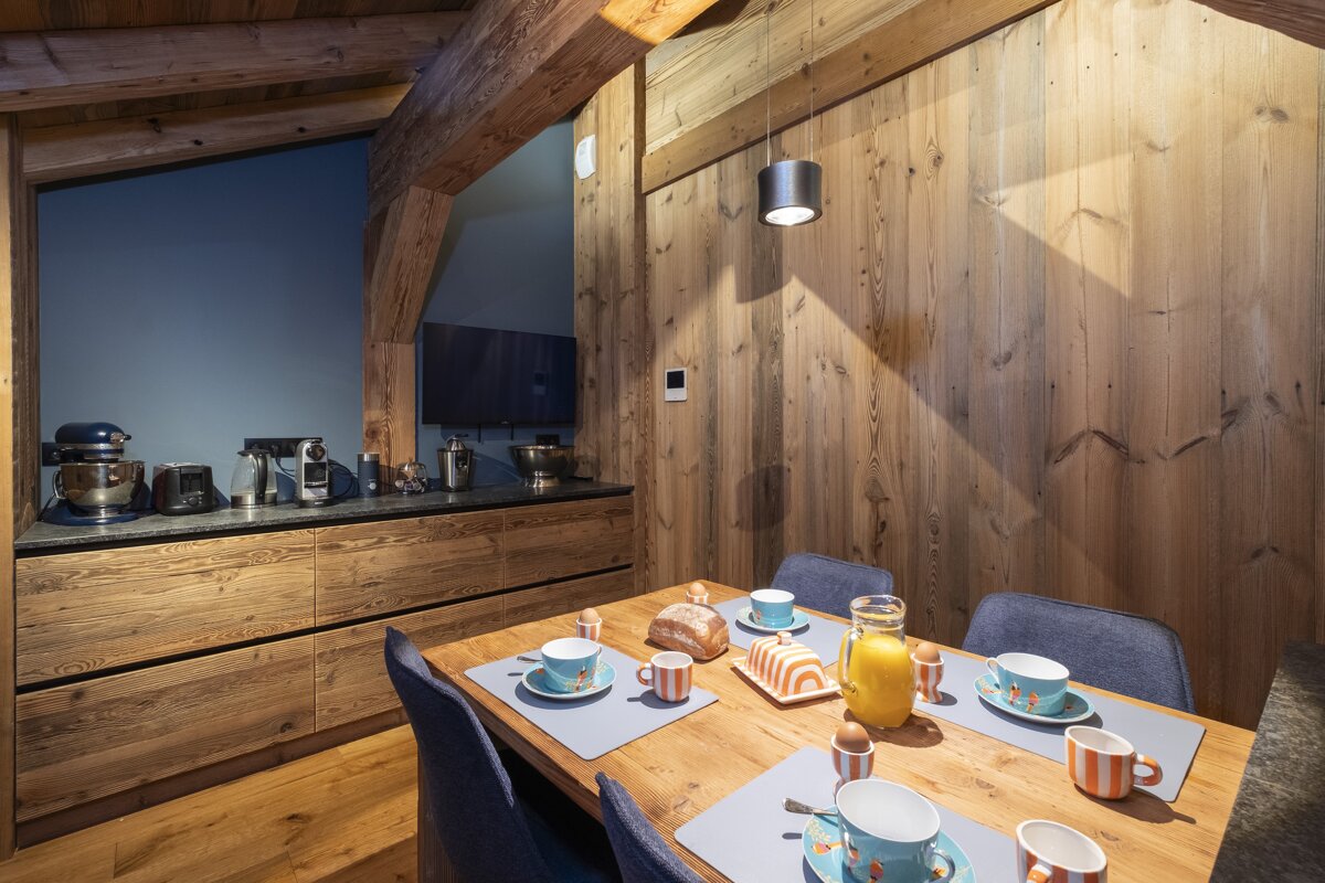 A cozy wooden chalet-style dining area with breakfast set for four, next to a modern kitchen counter filled with appliances.