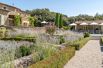A stone house with a swimming pool surrounded by flowers and umbrellas