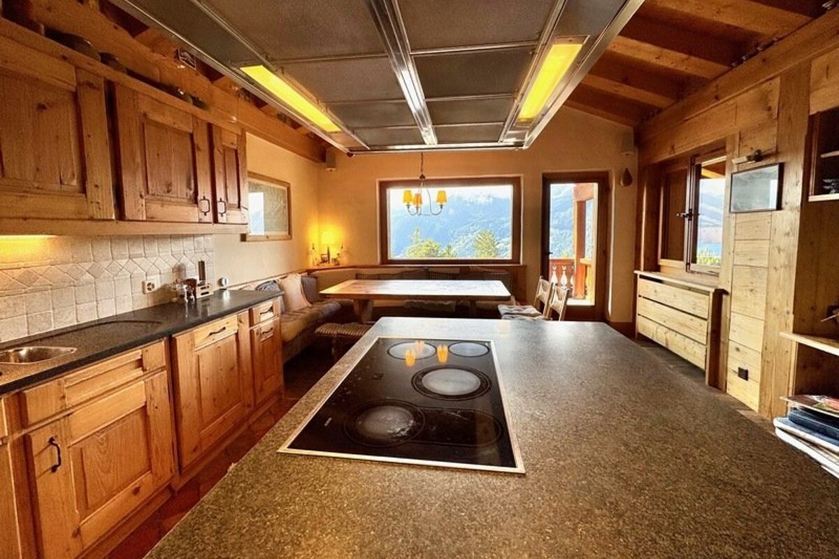 Cozy cabin kitchen with rustic wood cabinetry, a large island with a cooktop, and a dining area offering scenic mountain views.