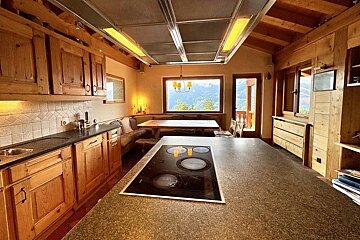 Cozy cabin kitchen with rustic wood cabinetry, a large island with a cooktop, and a dining area offering scenic mountain views.