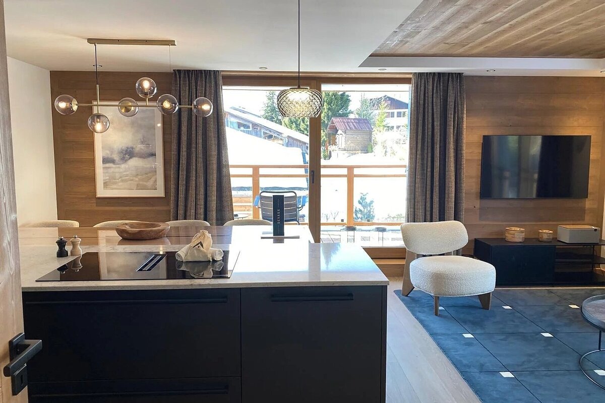 Modern chalet interior with an open kitchen, a cozy living area, and large balcony doors showing a snowy landscape.