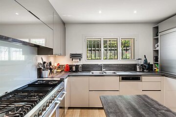 Modern kitchen with sleek beige cabinets, a large gas range, dark countertops, and a window above the sink.