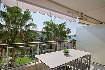 A white table and chairs on a balcony with palm trees in the background