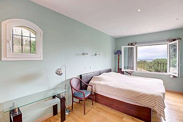 Serene mint green bedroom with a bed, glass desk, and a large open window revealing a sea view and balcony, plus an arched window.