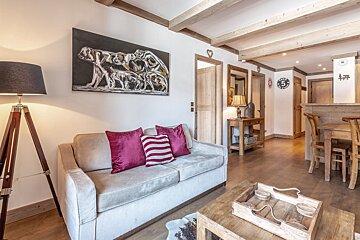 Rustic cabin living room featuring a grey sofa with pink pillows, a bear painting, exposed wooden beams, and a tripod floor lamp.