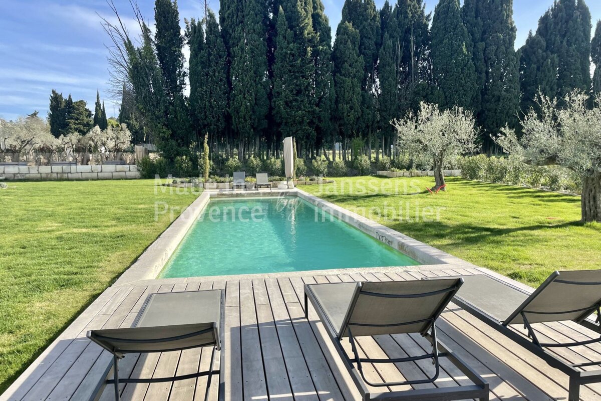 A large swimming pool is surrounded by lawn chairs and a wooden deck