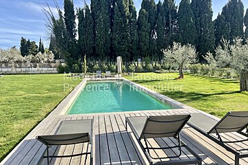 A large swimming pool is surrounded by lawn chairs and a wooden deck