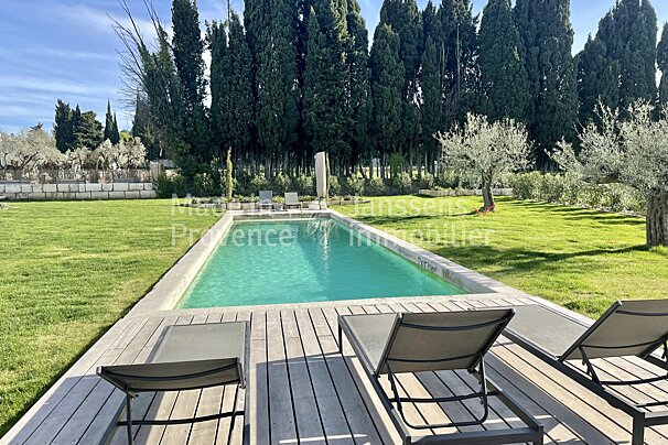 A large swimming pool is surrounded by lawn chairs and a wooden deck