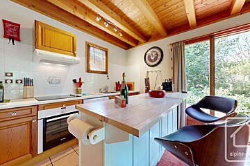 Bright kitchen featuring a wooden beamed ceiling, modern appliances, a kitchen island with bar stools, and a window offering a view of lush greenery.