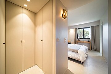 Modern interior with beige built-in closets on the left and a bright bedroom with a bed and window visible on the right.