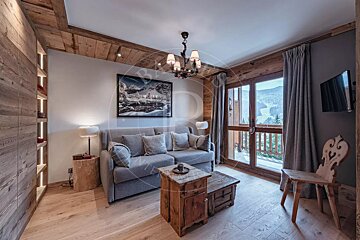 Rustic, cozy living room with a grey sofa, wooden coffee table, and large window overlooking a scenic mountain view.