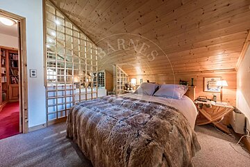 Cozy, wood-paneled attic bedroom featuring a large bed with a furry blanket and a decorative grid partition. A doorway leads to another room.