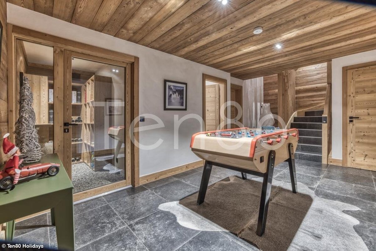Rustic chalet game room featuring a foosball table on a hide rug, wooden ceilings, stone tile flooring, and stairs.
