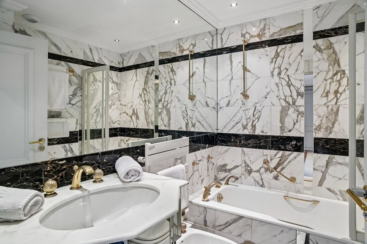 Elegant marble bathroom featuring a white vanity sink and a matching marble-tiled bathtub, accented with gold fixtures.