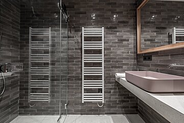 Modern bathroom with dark gray brick tiles, a glass shower, white towel warmer, and a pink sink on a concrete counter.