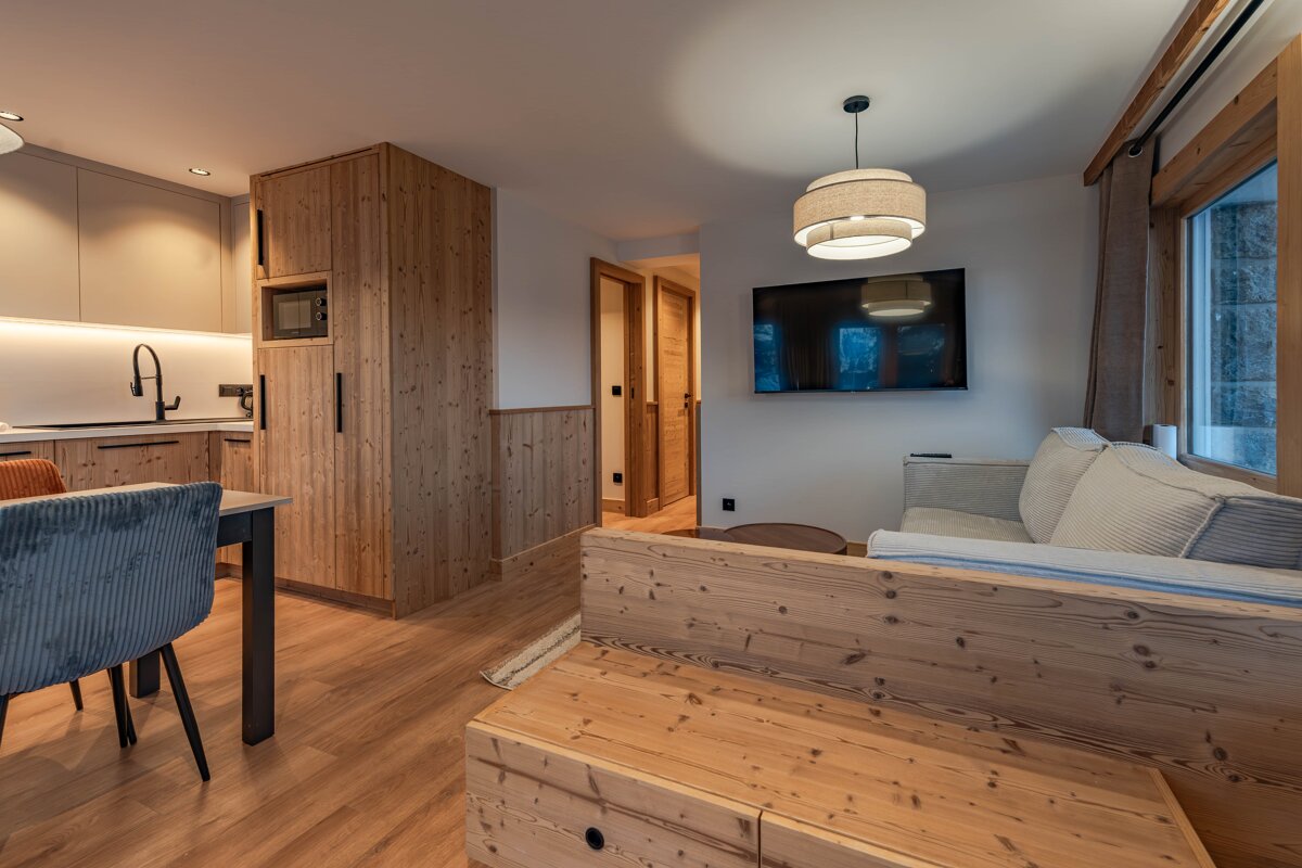 Cozy modern alpine apartment interior with warm wood cabinetry, a comfortable sofa, TV, and an open kitchen/dining space.
