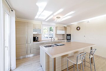 Bright, modern kitchen with light wood cabinets, a central island with a sink and bar stools, and stainless steel appliances.