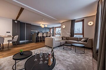 Modern open-plan apartment featuring a cozy living area with a beige sectional, wooden floors, and a sleek kitchen with bar stools.