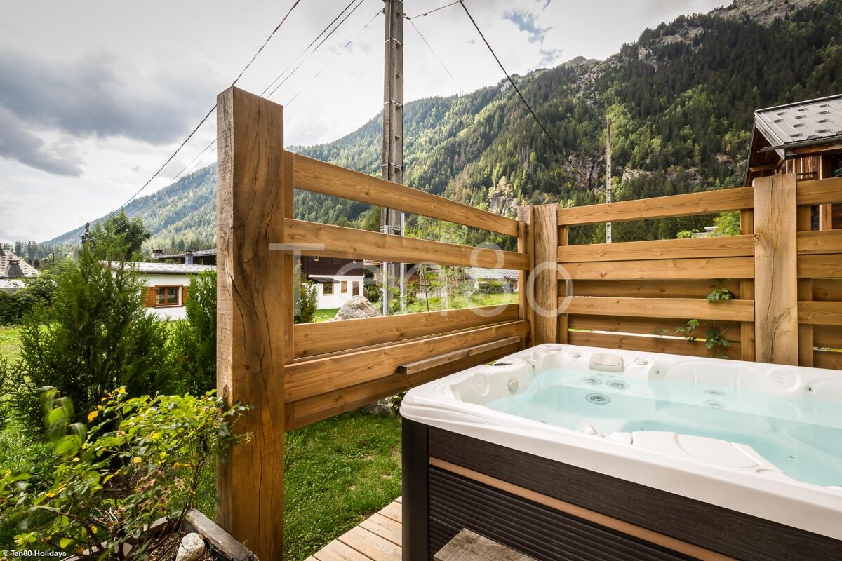 A hot tub is surrounded by a wooden fence and mountains in the background