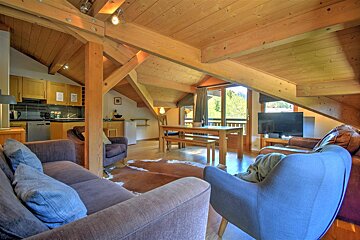 Cozy rustic chalet interior with exposed wood beams, comfortable sofas, a dining table, and a kitchenette.