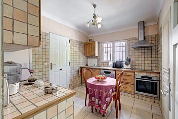 A cozy kitchen with checkered tiled walls, wooden cabinets, a small dining table with a pink tablecloth, and modern appliances.