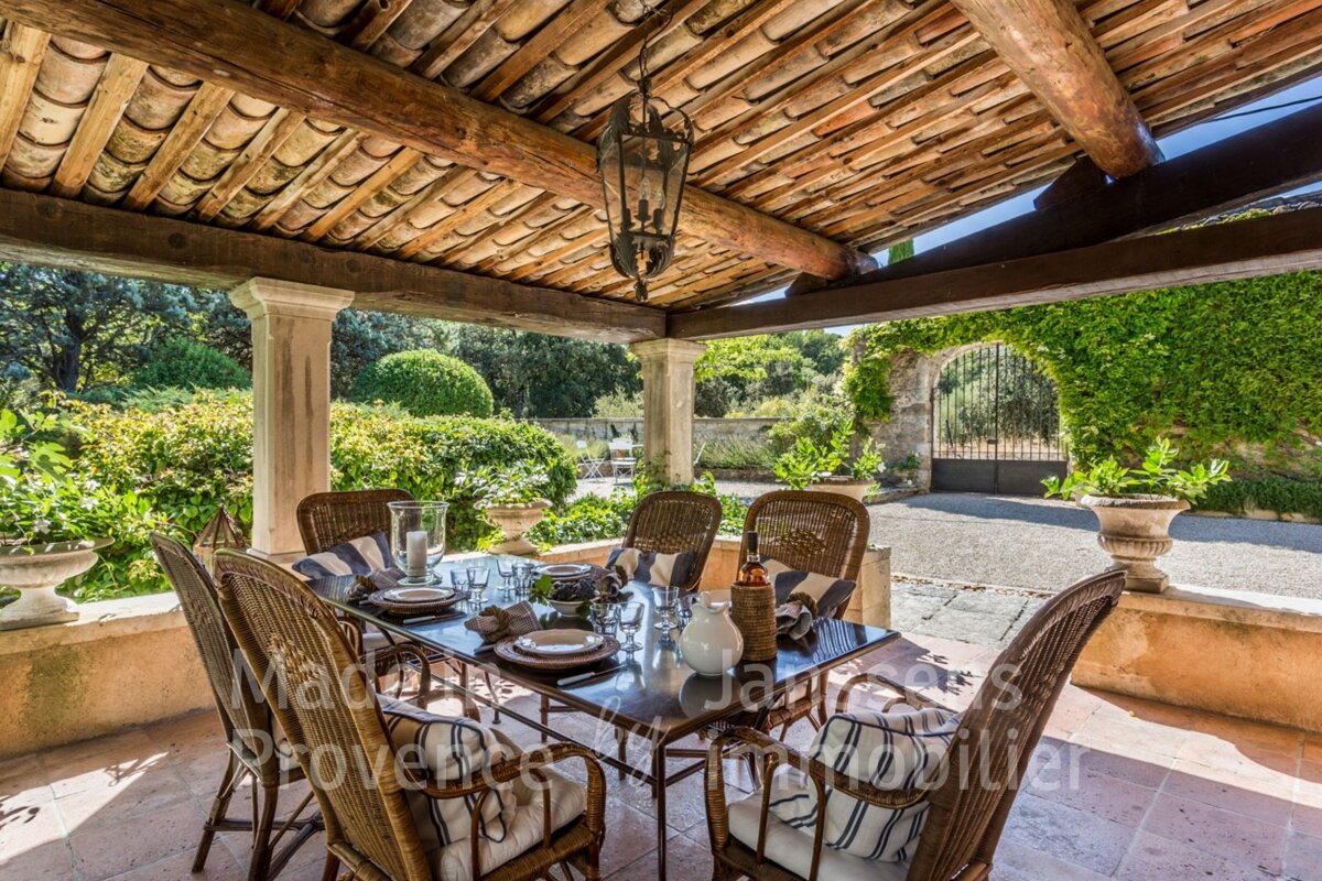 A table and chairs under a wooden roof that says provence immobilier