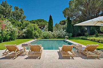 A large swimming pool surrounded by chairs and a white umbrella