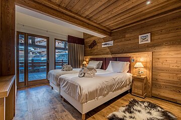 Cozy wood-paneled bedroom with two single beds, a balcony access, and a rustic, chalet-style interior.