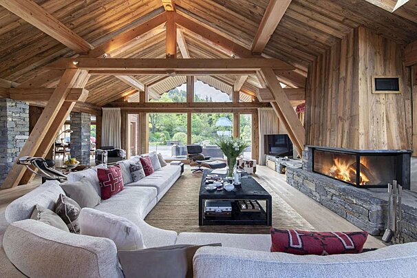 A spacious, luxurious rustic-modern living room with vaulted wooden ceilings, a sleek fireplace, and a large sectional sofa, overlooking nature.