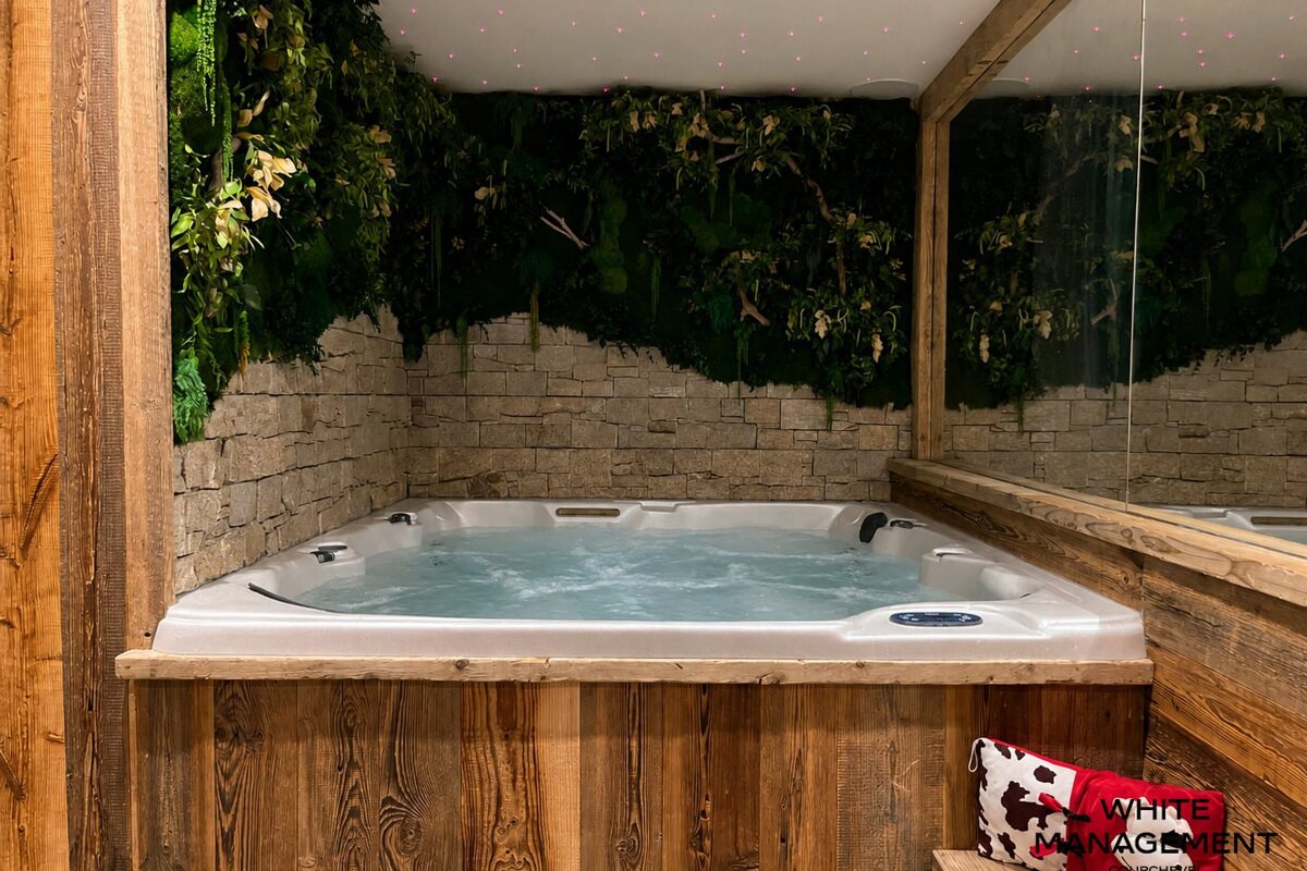Cozy indoor jacuzzi framed in rustic wood with a stone wall covered in lush greenery and a starry ceiling.