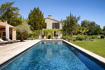 A large swimming pool is surrounded by lawn chairs and a house