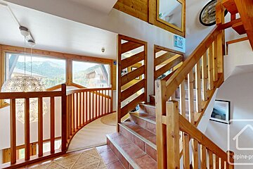 Warm, rustic wooden interior featuring multi-level stairs, curved railing, and large windows with a mountain view.