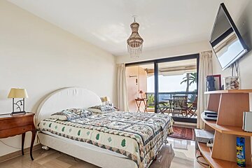 A bedroom featuring a bed with a pattern bedcover, a chandelier, and a balcony.