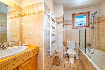 A tiled bathroom featuring a wooden vanity, a heated towel rack, a toilet, and a bathtub with a glass screen.