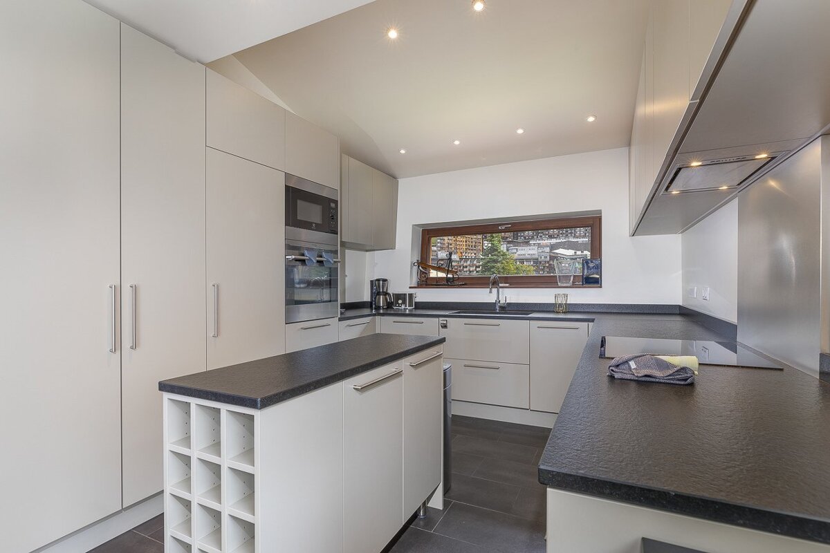Modern kitchen with sleek white cabinetry, black countertops, an island with a built-in wine rack, and a window with an outdoor view.
