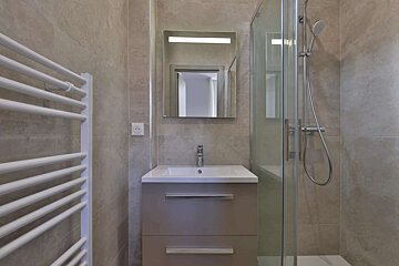 A modern bathroom with beige tiled walls, a white towel warmer, a vanity with sink, a lighted mirror, and a glass-enclosed shower.