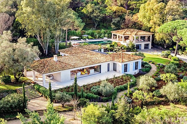 High-angle view of a luxury Mediterranean villa with tiled roofs, surrounded by lush gardens, walkways, and a pool.