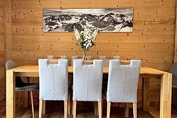 Wooden dining table with grey chairs, a vase of white flowers, and a black-and-white mountain panorama on a wood-paneled wall.