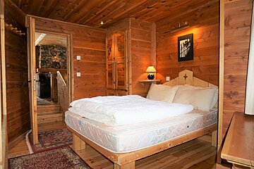 A cozy rustic bedroom with knotty pine wood paneled walls, ceiling, and built-in wardrobes, featuring a white bed with pillows.