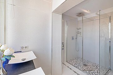 Modern bathroom featuring a white vessel sink on a dark vanity and a large glass-enclosed shower with mosaic tiling.