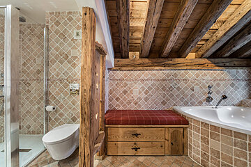 A bathroom with a toilet a bathtub and a wooden bench